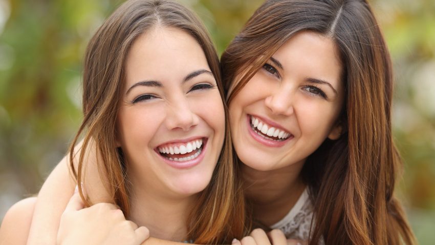 Two women friends laughing with a perfect white teeth with a green background